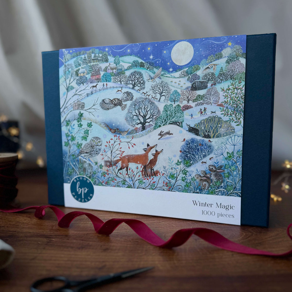 A boxed jigsaw puzzle titled "Winter Magic" stands on a wooden table. The front of the box shows a detailed winter landscape illustration with snow, trees, foxes with other wildlife, and a full moon.