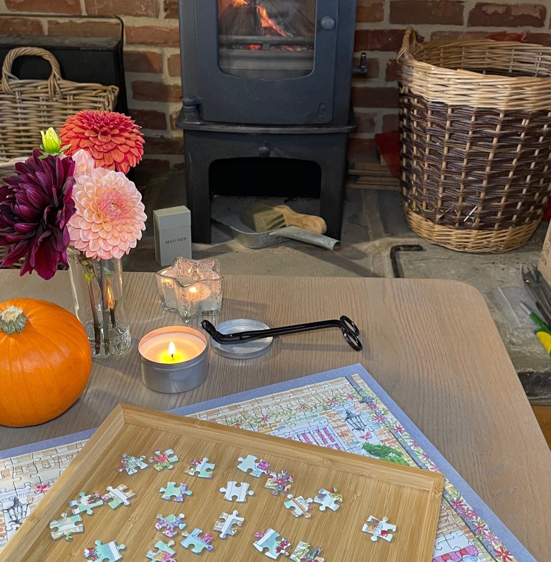 Le Cafe Puzzle with sorting tray on a table in front of a lit wood burner with flowers and a pumpkin