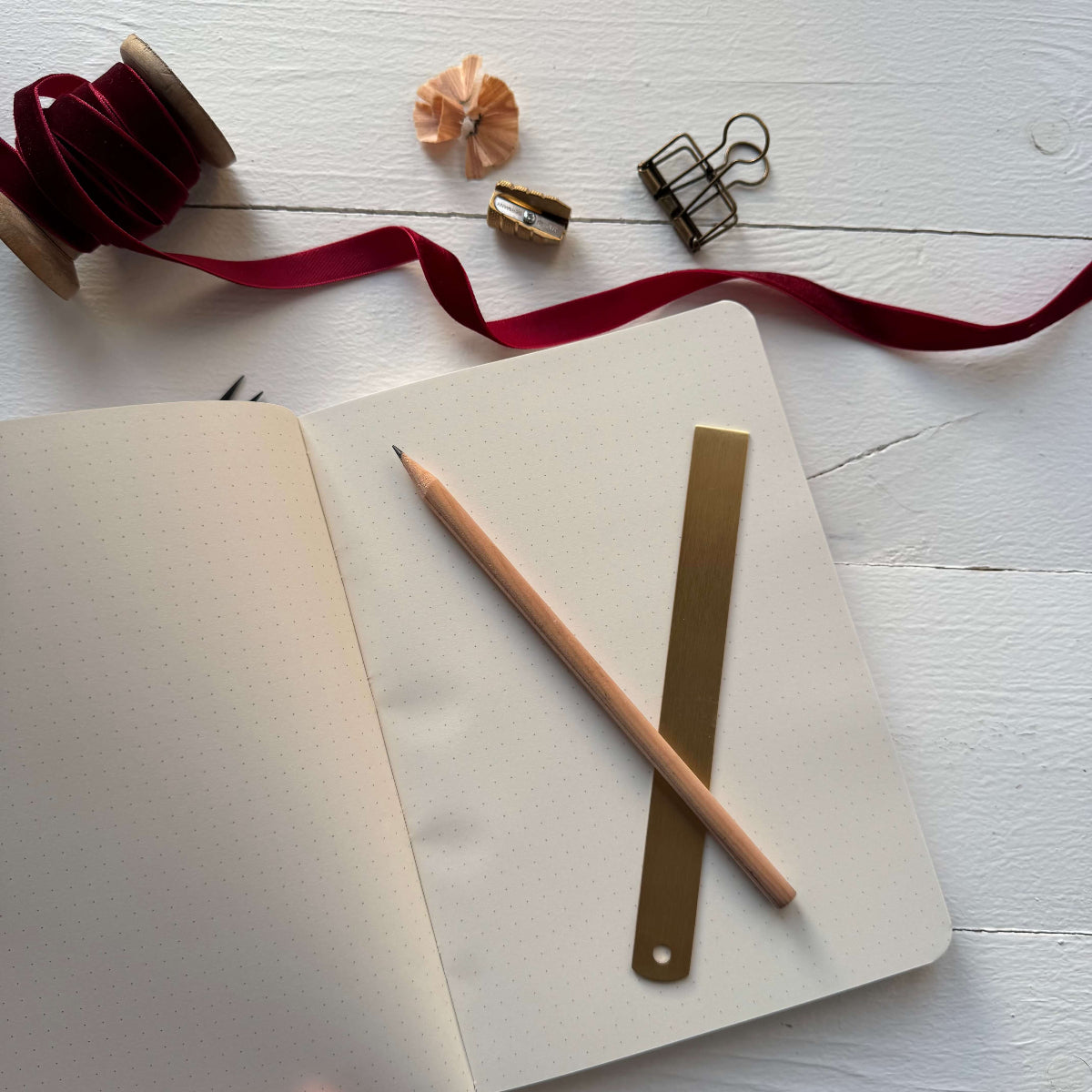 Open notebook with a pencil and ruler on a white wooden surface with decorative ribbons and clips.